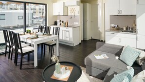 A modern kitchen with white cabinets, a dining area with a white table and chairs, and a gray sofa with cushions. - Hausboot in Boltenhagen (Boltenhagen)