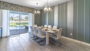 Een eetruimte met een tafel gedekt voor vier personen, een moderne kroonluchter en uitzicht op een zwembad door grote ramen.