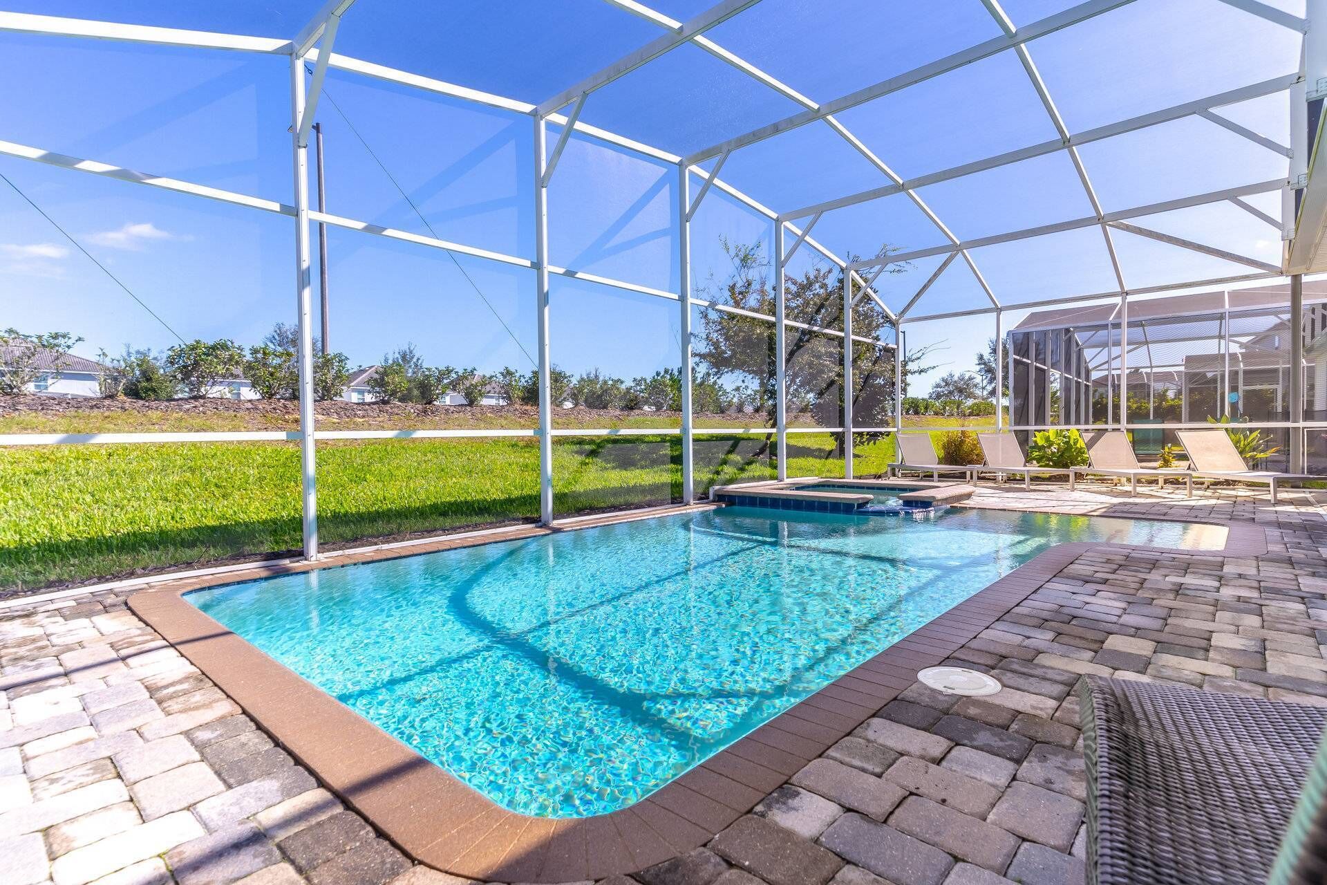 A covered swimming pool with clear blue water, surrounded by a glass enclosure, and a brick patio area with lounge chairs.