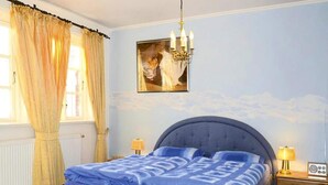 A bedroom with a bed, a chandelier, a painting, and a nightstand with a radio. - Ferienwohnung in Oevenum auf Foehr (Oevenum)