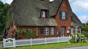 A traditional thatched-roof house with a white picket fence, brick walls, and green shutters. - Ferienwohnung in Oevenum auf Foehr (Oevenum)