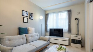 A modern living room with a sofa, a coffee table, a TV, and a ceiling light fixture. - UNAKITE 102 (Sapporo)