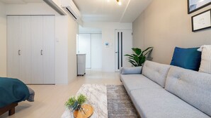 A modern living room with a grey sofa, a wooden coffee table, and a large plant. - UNAKITE 102 (Sapporo)
