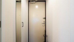 A narrow hallway with a closed door, a metal rack, and a light switch on the wall. - UNAKITE 102 (Sapporo)