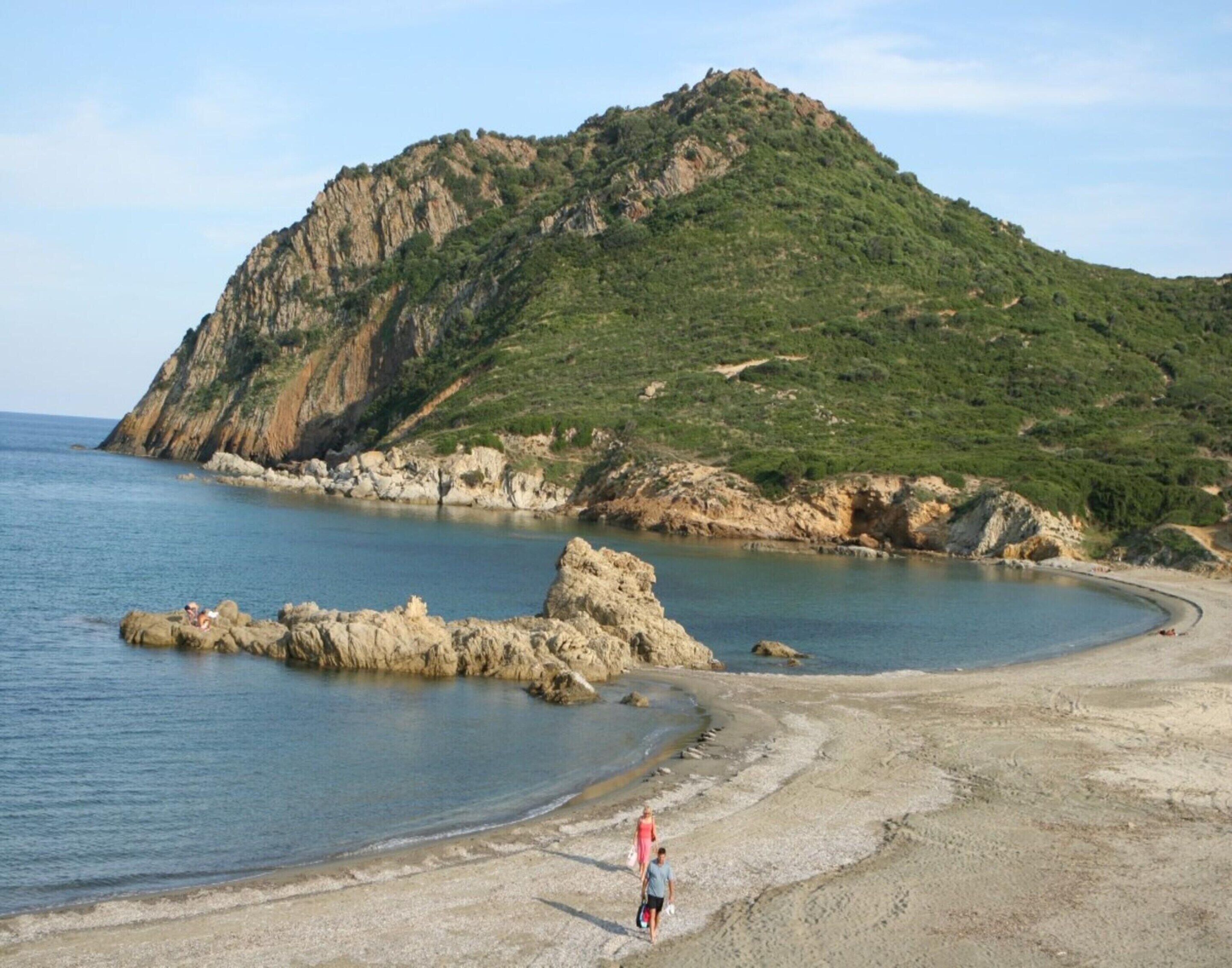 Una playa con formaciones rocosas y una colina al fondo.