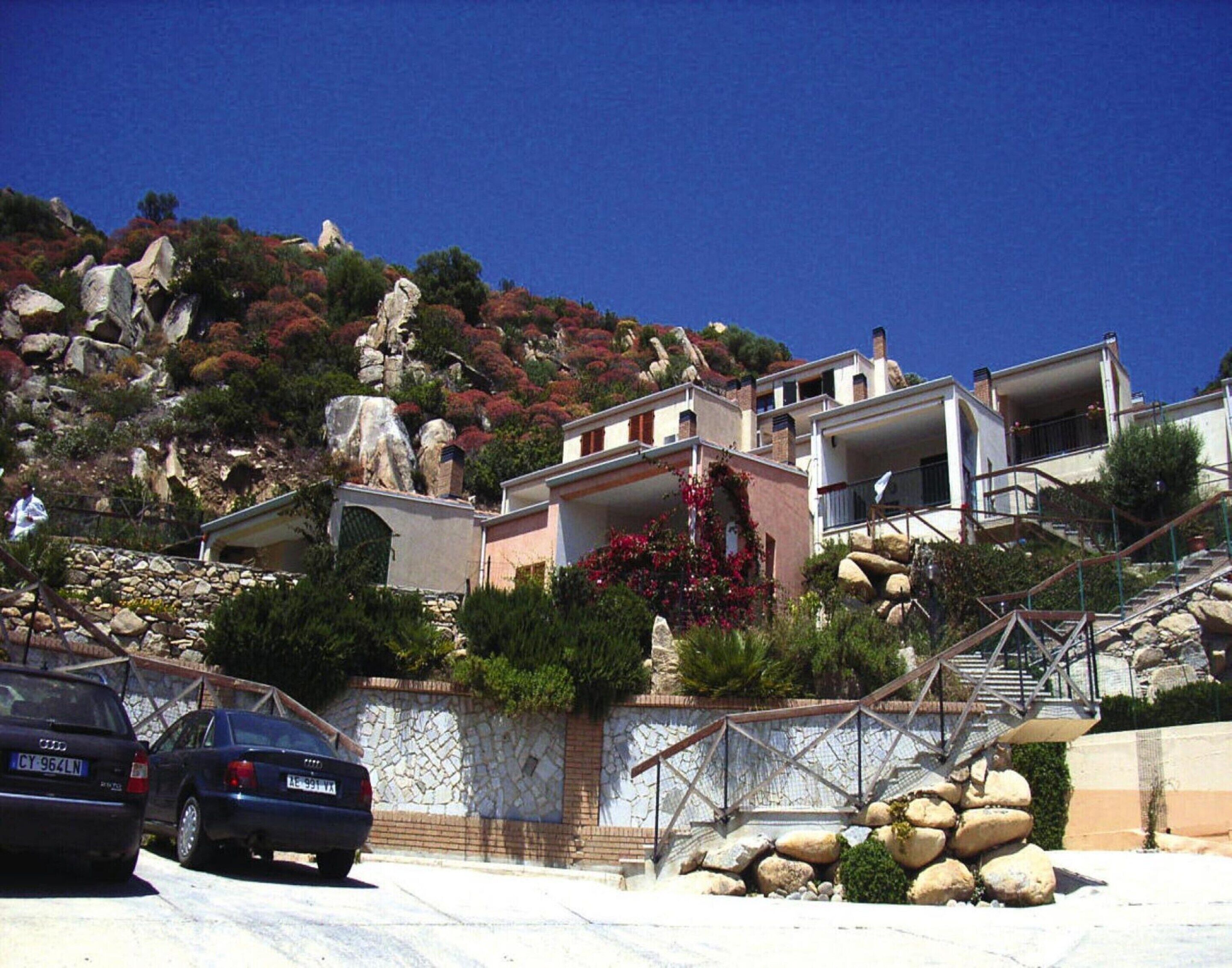 A hillside property with a stone wall, a staircase, and a car parked in front.