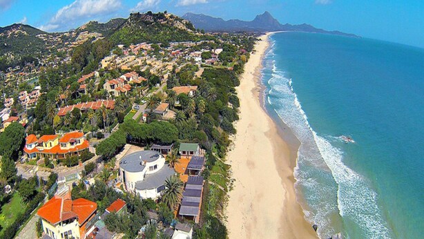 An aerial view of a coastal town with a beach, houses, and a hill with a fort-like structure. - Apartment in Costa Rei With Stunning Sea View (Muravera)