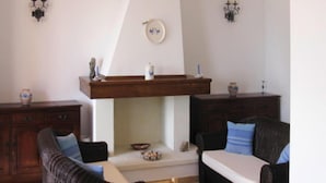 A living room with two dark brown sofas, a wooden coffee table, and a woven chair. There are wall-mounted sconces and a decorative plate above a fireplace. - Apartment in Costa Rei With Stunning Sea View (Muravera)
