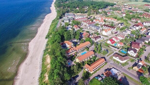 An aerial view of a coastal town with a beach, residential buildings, and a mix of houses and larger structures. - Cottage in Rewal Near Baltic Sea Beach (Rewal)