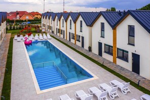 En swimmingpool med liggestole og en vandrutsjebane, omgivet af moderne bygninger med nummererede døre.
