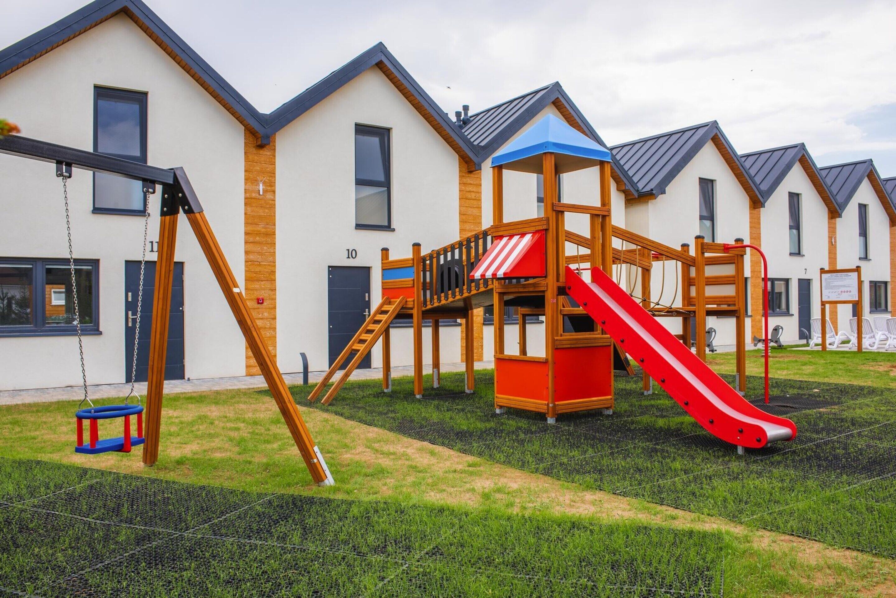 A playground with a slide and swings, surrounded by modern houses with similar architecture.