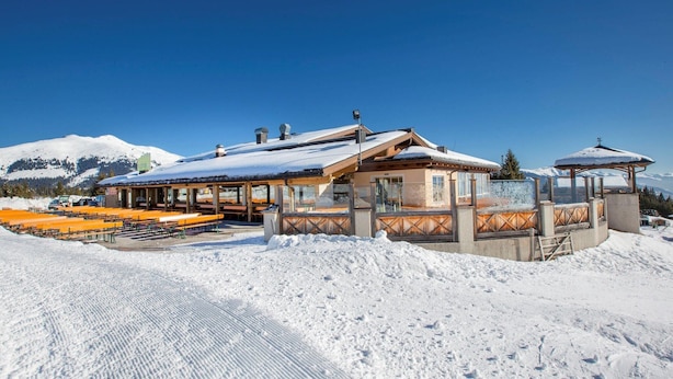A snow-covered lodge with outdoor seating and a mountain backdrop.