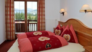 A hotel room with a bed, a wooden headboard, two wall-mounted lamps, a window with curtains, and a view of mountains.