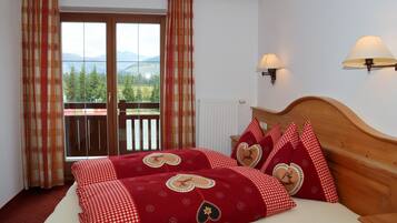 A hotel room with a bed, a wooden headboard, two wall-mounted lamps, a window with curtains, and a view of mountains.