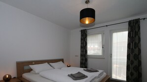 A neatly made bed with pillows and a blanket, a bedside table with a lamp, and a window with curtains. - Apartment in Hippach Near Mayrhofen Ski Area (Hippach)