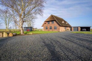 A large house with a gravel driveway, a garage, and a tree in the foreground. - Holiday Apartment in Tumlauer Koog (Tumlauer Koog)