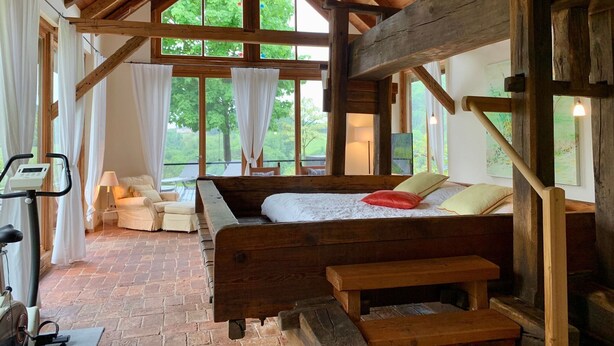 A rustic wooden room with a bed, a bench, a treadmill, and large windows. - Chalet in Styria With Pool & Panoramic Views (Fehring)