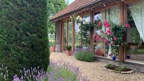 A house with large glass windows, a gravel driveway, and various plants including lavender and flowering bushes. - Chalet in Styria With Pool & Panoramic Views (Fehring)