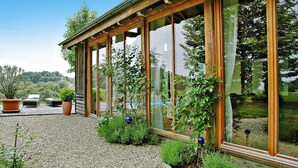 A modern house with large glass windows, a wooden deck, and a gravel pathway. - Chalet in Styria With Pool & Panoramic Views (Fehring)
