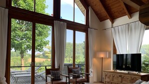 A spacious living room with large windows, a flat-screen TV, and comfortable seating. - Chalet in Styria With Pool & Panoramic Views (Fehring)