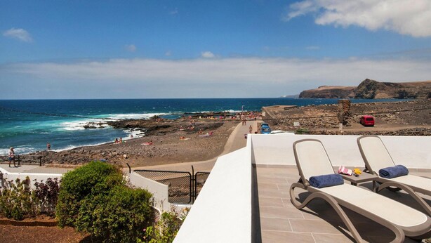 Une plage avec vue sur la mer, des chaises longues, un terrain rocheux et un ciel dégagé.