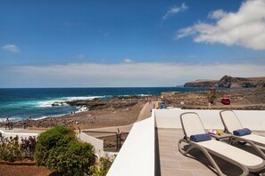 A beach view with lounge chairs, rocky terrain, and a clear sky.
