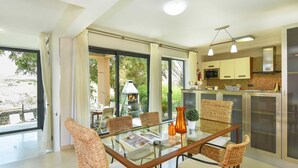 A modern kitchen with a glass dining table, wicker chairs, and a view of the outdoors. - Holiday Home, Maspalomas (San Bartolomé de Tirajana)