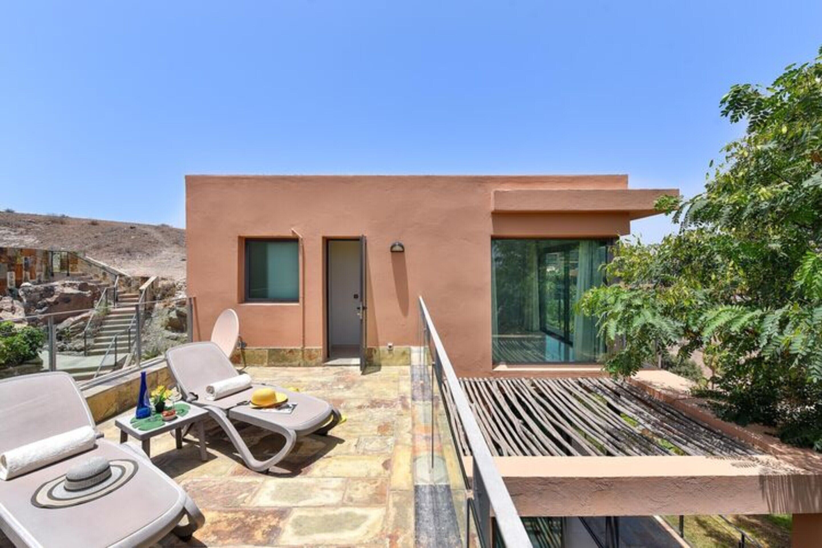 A modern building with a flat roof, a glass door, and a small balcony with lounge chairs.