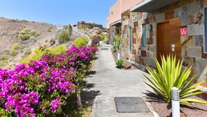 A pathway lined with vibrant bougainvillea flowers leading to a building with stone and stucco exterior walls, a wooden door, and a sign with a 'W' symbol. - Holiday Home, Maspalomas (San Bartolomé de Tirajana)