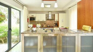 A modern kitchen with a granite countertop, stainless steel appliances, and a view of greenery outside. - Holiday Home, Maspalomas (San Bartolomé de Tirajana)