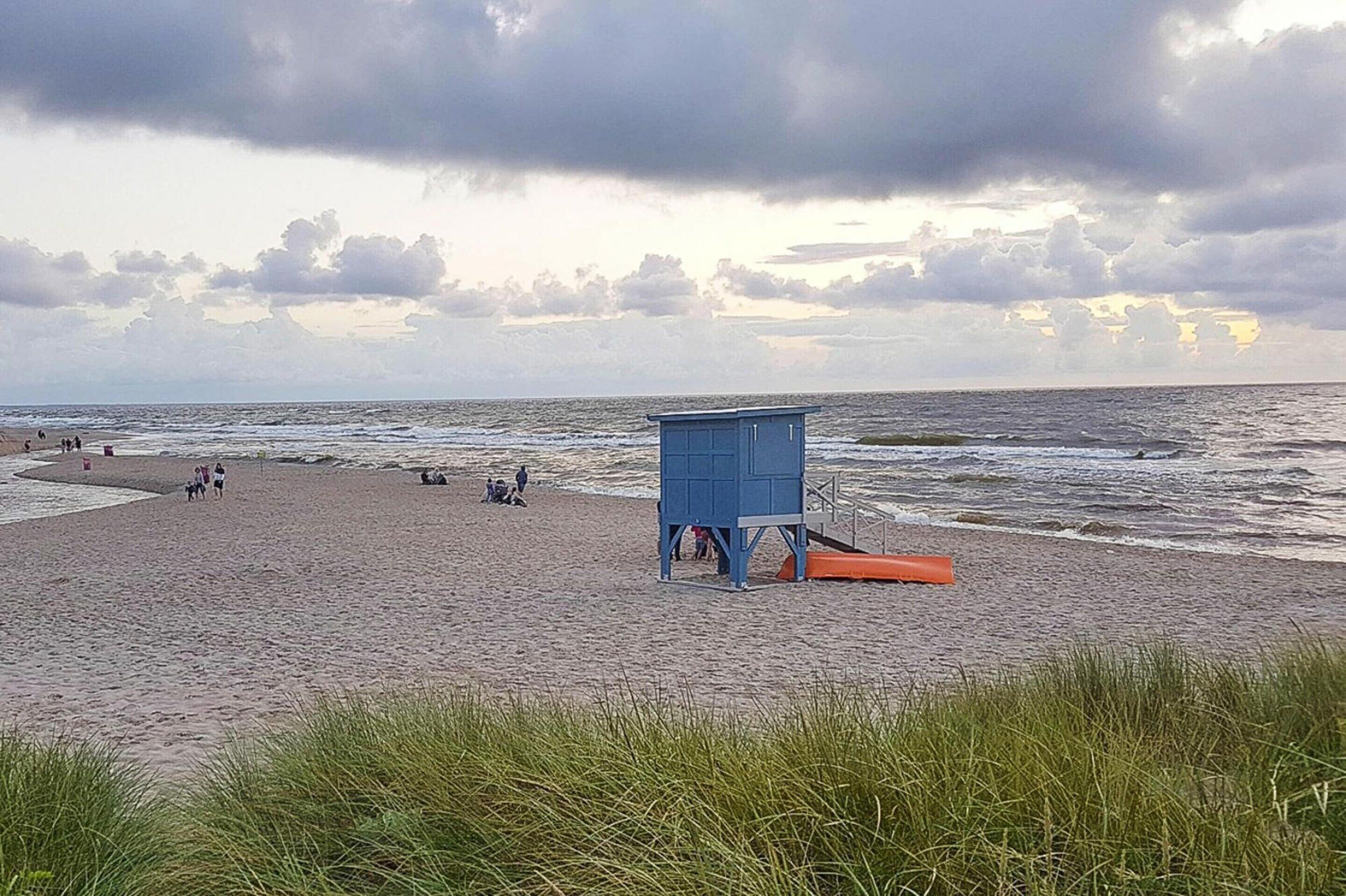 Una playa con una torre de salvavidas, olas y gente.