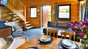A wooden cabin interior with a dining area, a sofa, a staircase, and a television. - Comfortable Holiday Homes With a Fireplace (Darlowo)