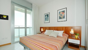 A hotel room with a bed, two bedside tables, a nightstand, a window, and two framed pictures on the wall. - Apartments Torre del Sole, Bibione Spiaggia (San Michele al Tagliamento)