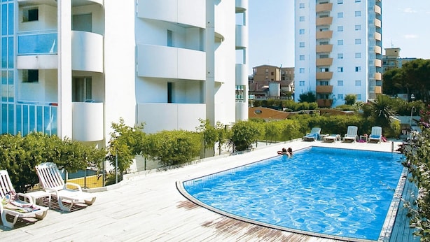 A modern building with a swimming pool, lounge chairs, and a clear view of the surrounding area. - Apartments Torre del Sole, Bibione Spiaggia (San Michele al Tagliamento)