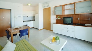 A compact kitchen with white cabinets, a wooden countertop, and a built-in TV. - Apartments Torre del Sole, Bibione Spiaggia (San Michele al Tagliamento)