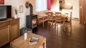 Un salon chaleureux avec une cheminée, des meubles en bois, un téléviseur et un coin repas, avec une cuisine en arrière-plan.
