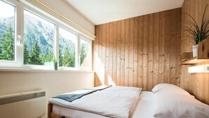 Une chambre avec un lit en bois, un radiateur, une fenêtre donnant sur la montagne et une plante posée sur le rebord de la fenêtre.