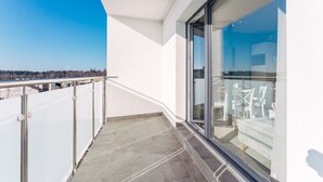 En balkon med frit udsyn over bybilledet, en glasdør der fører til en opholdsstue indendørs, og en hvid facade.