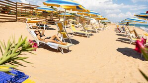 Ein Strand mit Reihen von Liegestühlen und Sonnenschirmen, feinem Sand und blauem Himmel.