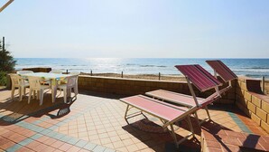 Eine Terrasse mit Tisch, Stühlen und zwei Liegestühlen, mit Blick auf das Meer.