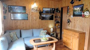 Una habitación acogedora con un sofá azul claro, una mesa de centro de madera y un armario de madera. Hay cuadros enmarcados en las paredes y un estante pequeño con adornos.