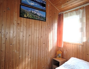 A wooden cabin room with a bed, a nightstand with a lamp, and two framed pictures on the wall. - Bungalow Near the Baltic Sea Beach (Kamien Pomorski)