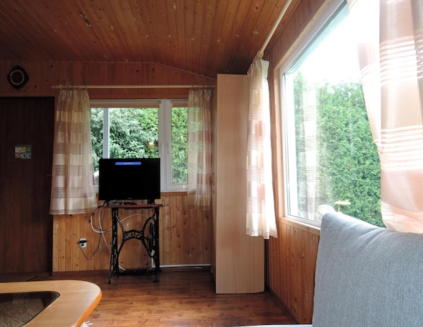 A wooden cabin interior with a television on a table, a sofa, and a window with curtains. - Bungalow Near the Baltic Sea Beach (Kamien Pomorski)