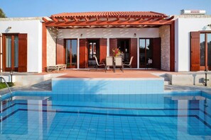 Ein modernes Gebäude mit Pool, großen Fenstern und einer Terrasse mit Gartenmöbeln.