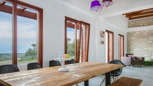 Un comedor amplio con una mesa de madera, sillas negras y un banco. Grandes ventanales ofrecen vistas al campo.