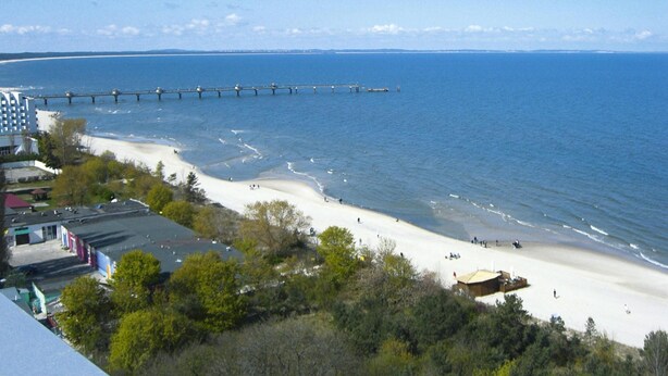 A beach with a pier extending into the sea, surrounded by buildings and greenery. - Detached Cottages by the Lake, Lubin (Miedzyzdroje)