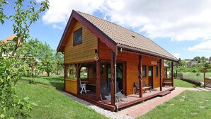 A wooden cabin with a porch, outdoor seating, and a clear view of the surrounding greenery. - Detached Cottages by the Lake, Lubin (Miedzyzdroje)