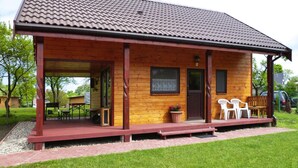 A wooden cabin with a tiled roof, a porch with chairs, and a small table. - Detached Cottages by the Lake, Lubin (Miedzyzdroje)