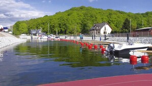 A marina with boats docked, a dock with red buoys, and a house in the background. - Detached Cottages by the Lake, Lubin (Miedzyzdroje)
