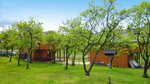 A grassy area with trees and a brick building with a covered porch. - Detached Cottages by the Lake, Lubin (Miedzyzdroje)